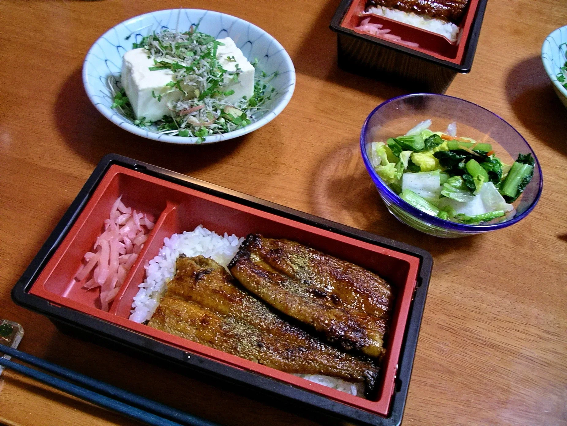 朱紅色漆器便當盒內放著蒲燒鰻魚和白飯，旁邊有冷豆腐與漬物