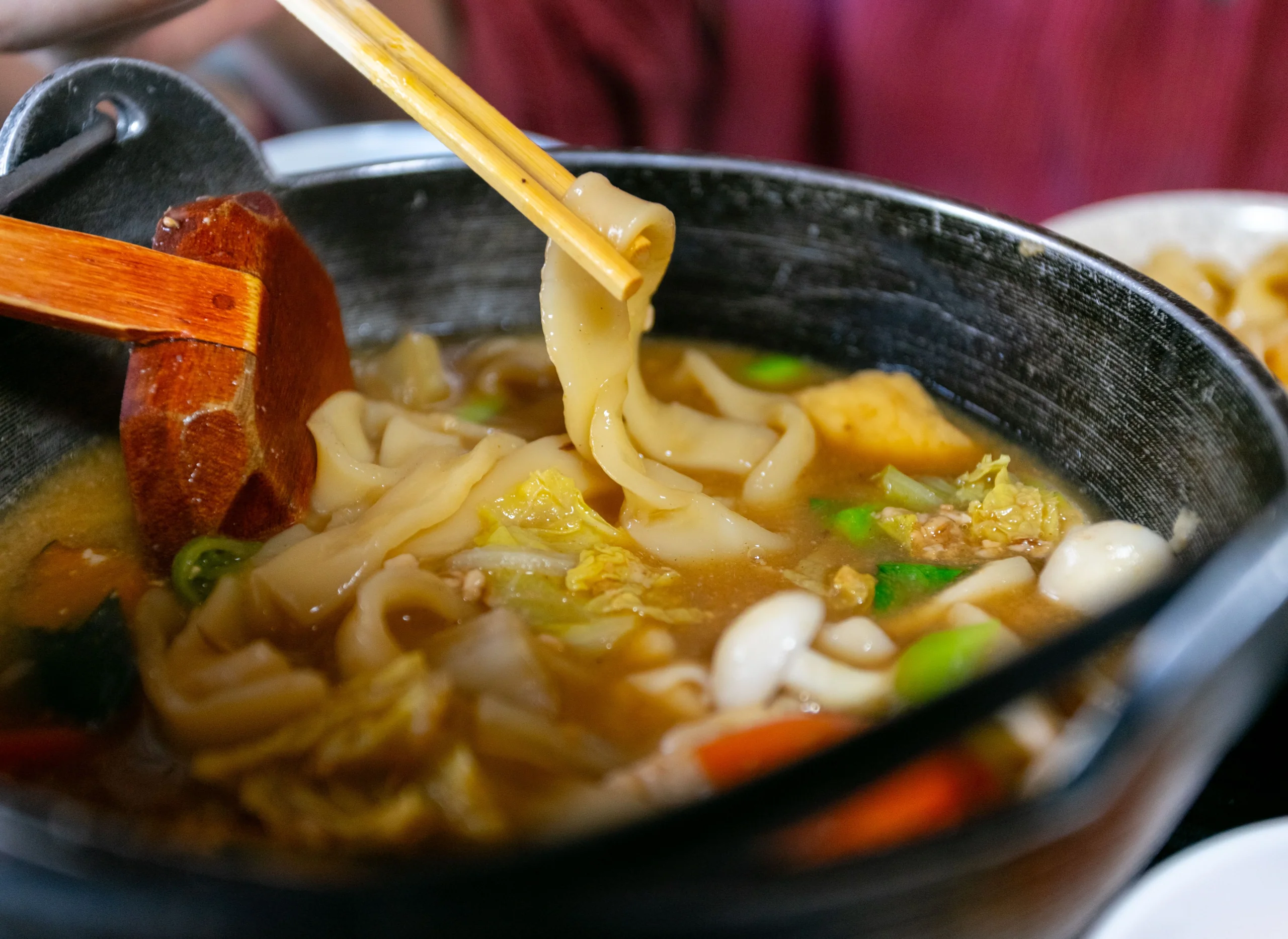 一碗烏龍麵湯麵近照，筷子夾起寬麵