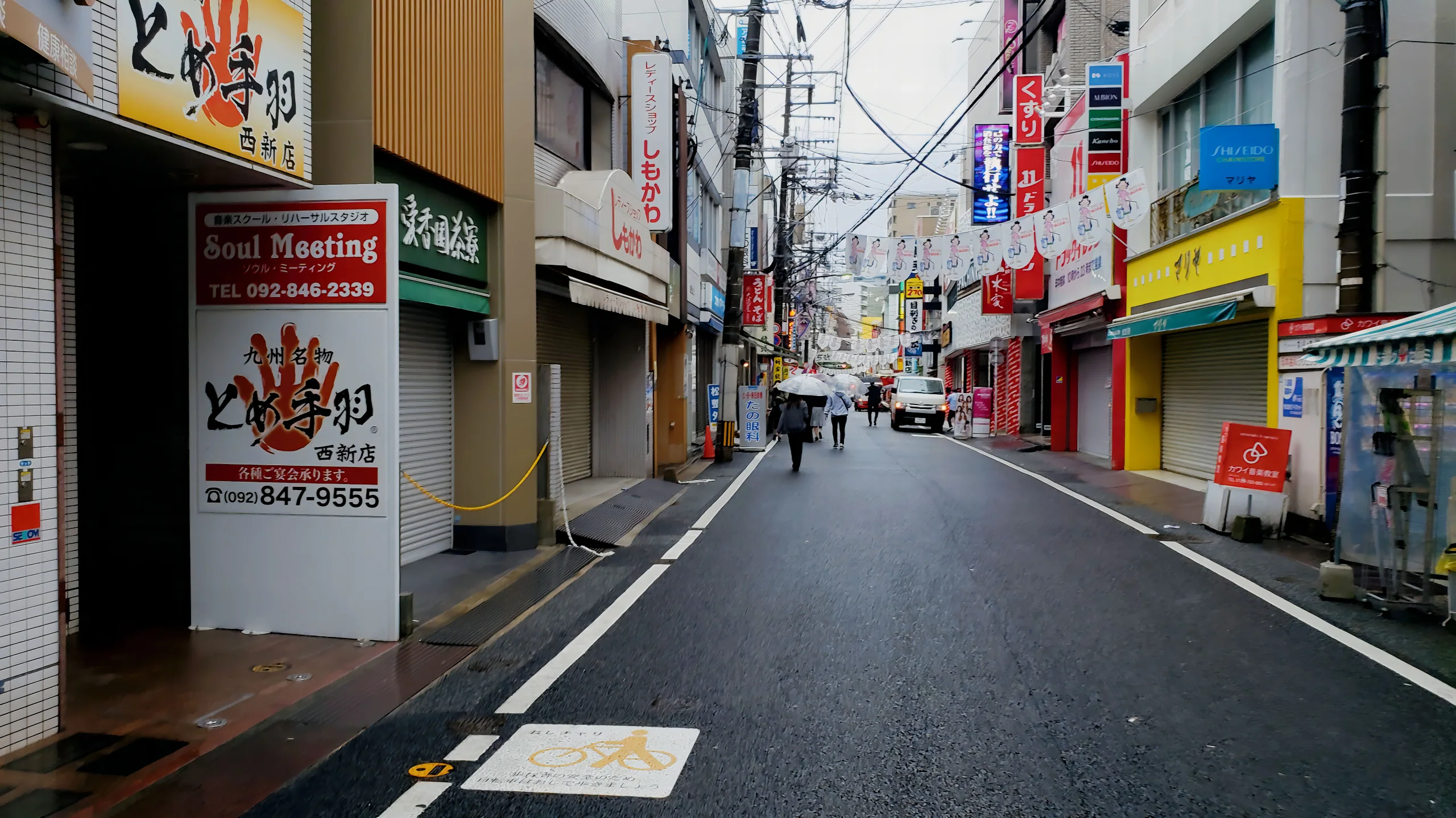 雨天的福岡市商店街街景，行人沿濕潤路面行走
