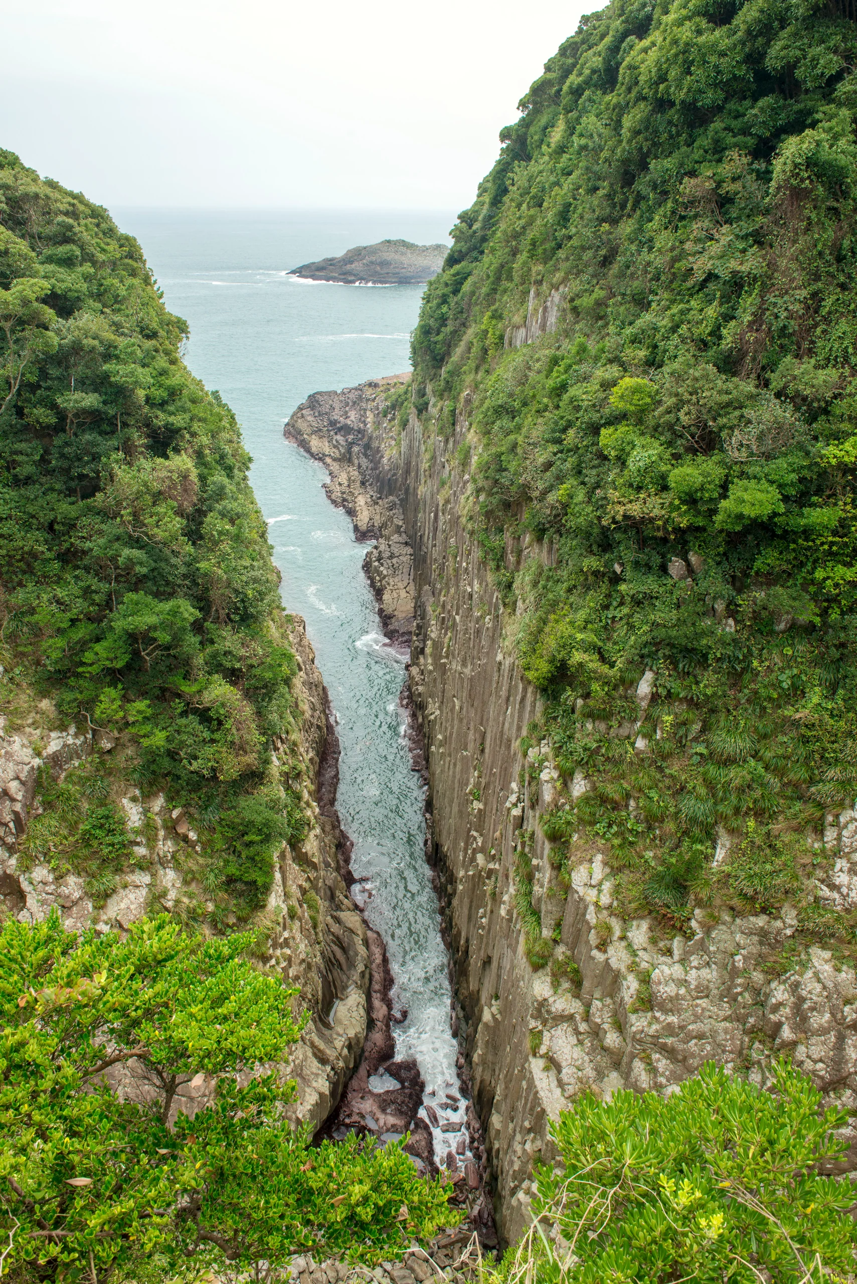 馬ヶ背海蝕峽的柱狀節理沿著兩側岩壁直落海面，崖頂覆著綠色植被