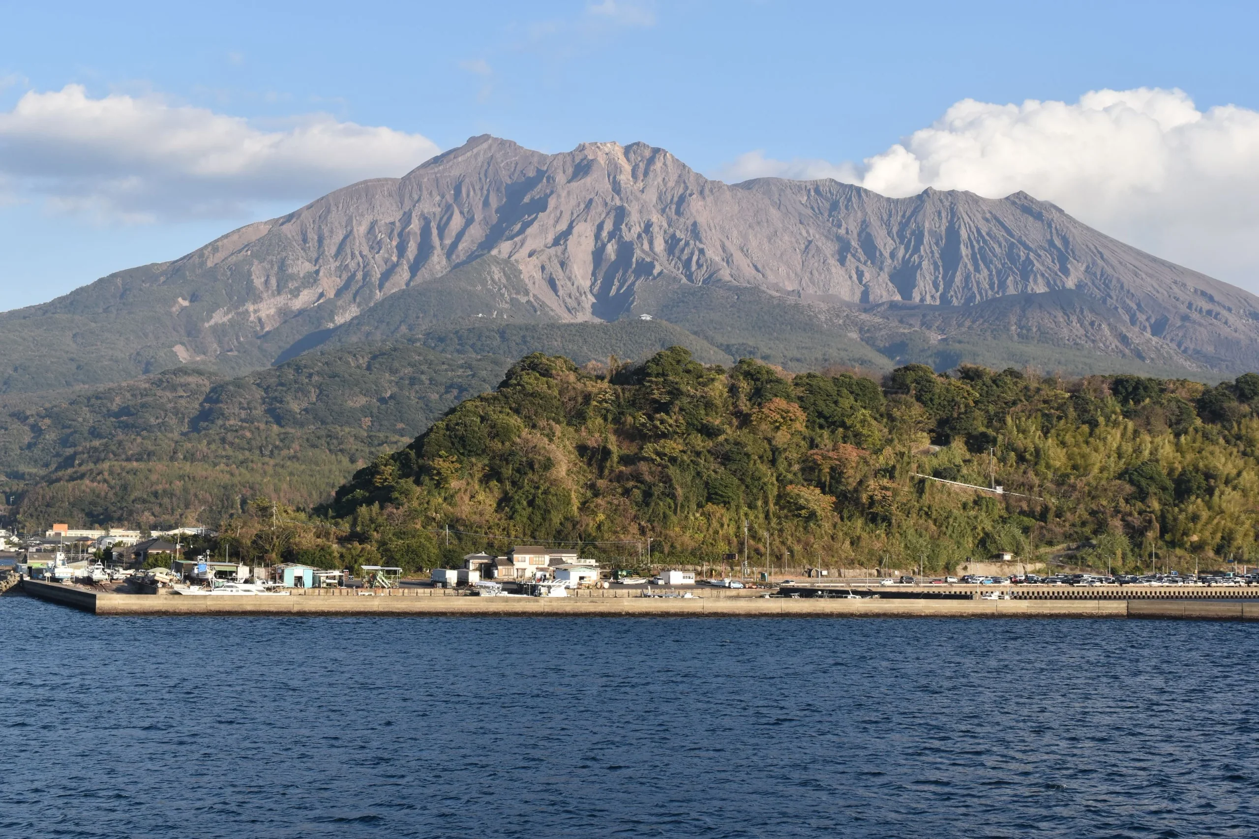 從渡輪上望向櫻島山體和島岸，遠處可見村落與港區