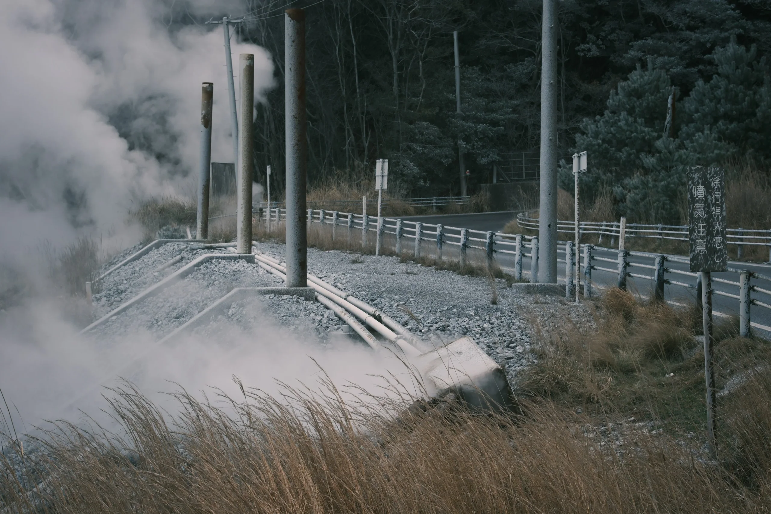 霧島山區道路旁的地熱蒸氣由地面升起，旁邊可見護欄和管線