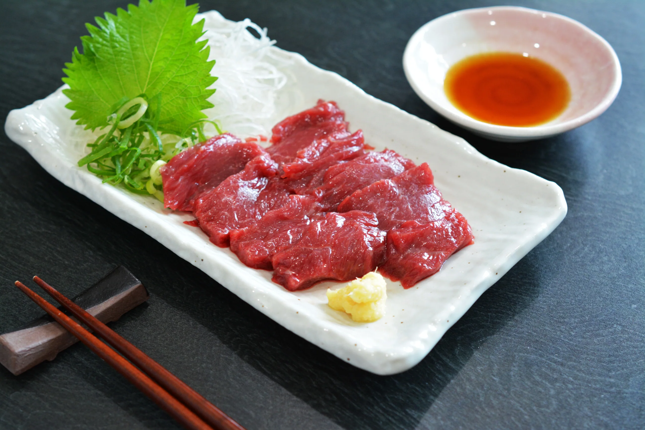 白色長盤上的赤身馬刺し切片，配紫蘇、蘿蔔絲、薑和醬油