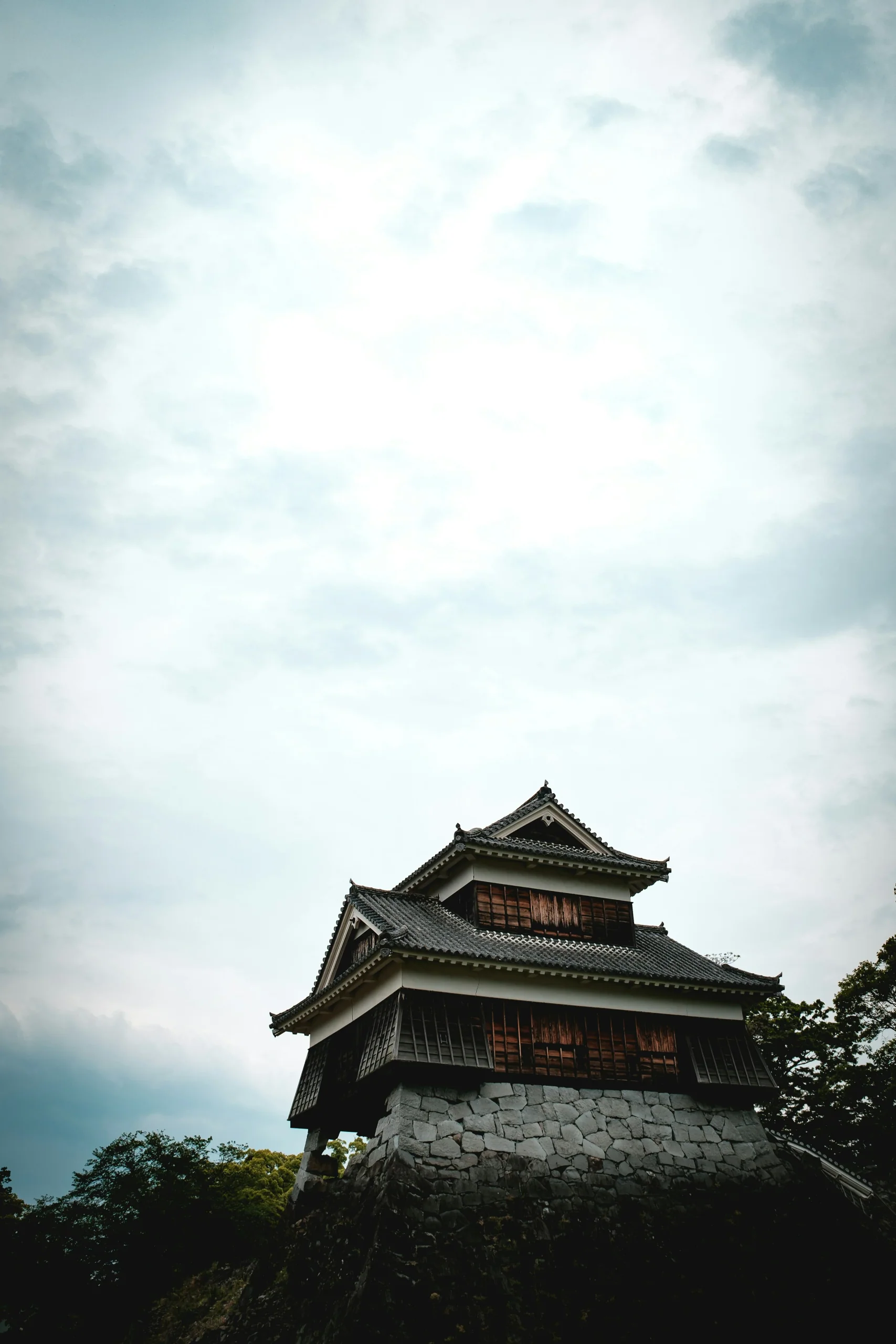熊本城天守由低處望上，塔樓與石垣映在晴朗天空下