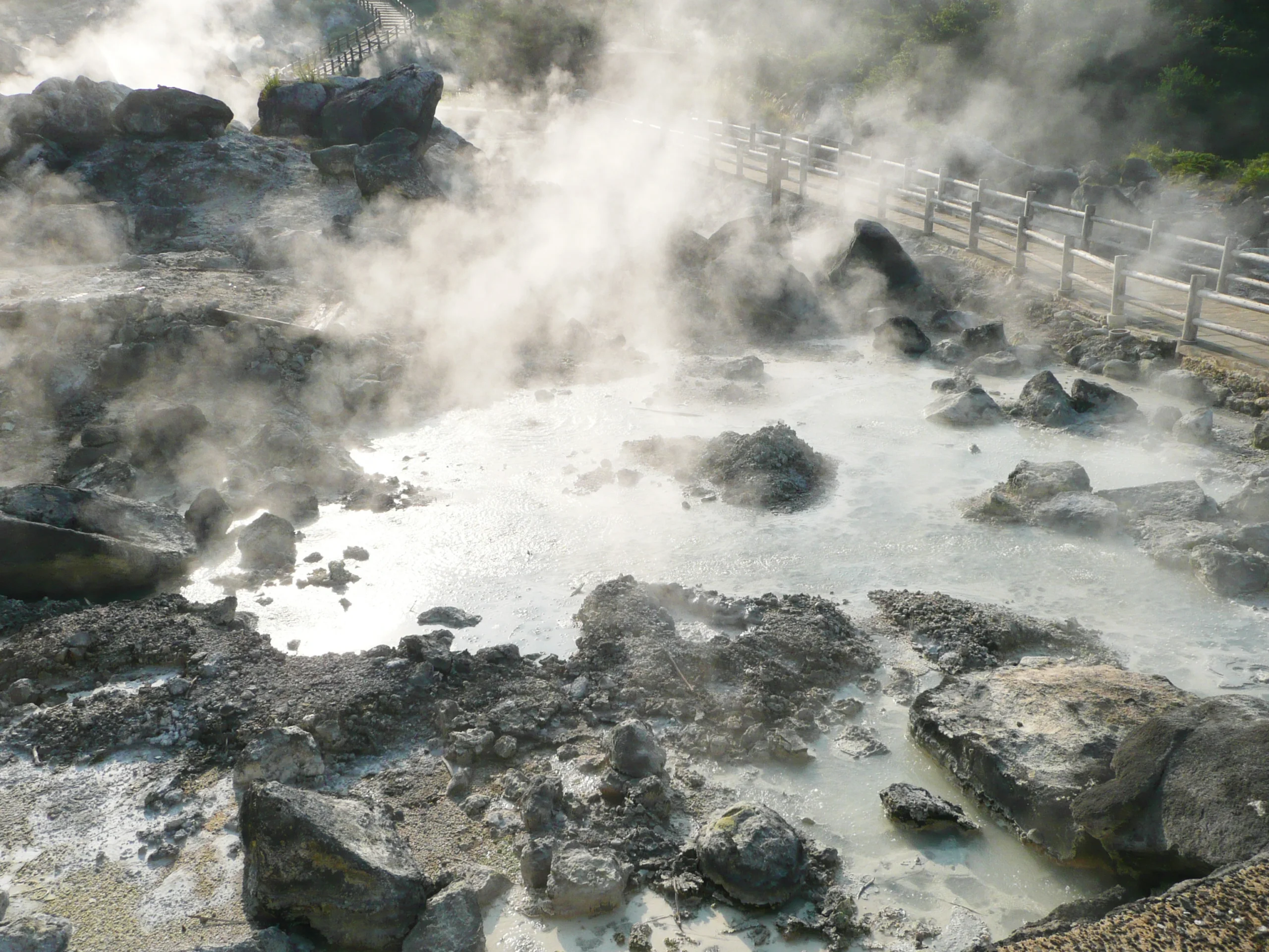 雲仙地獄岩石地帶冒出白色地熱蒸氣，木欄步道穿過溫泉區