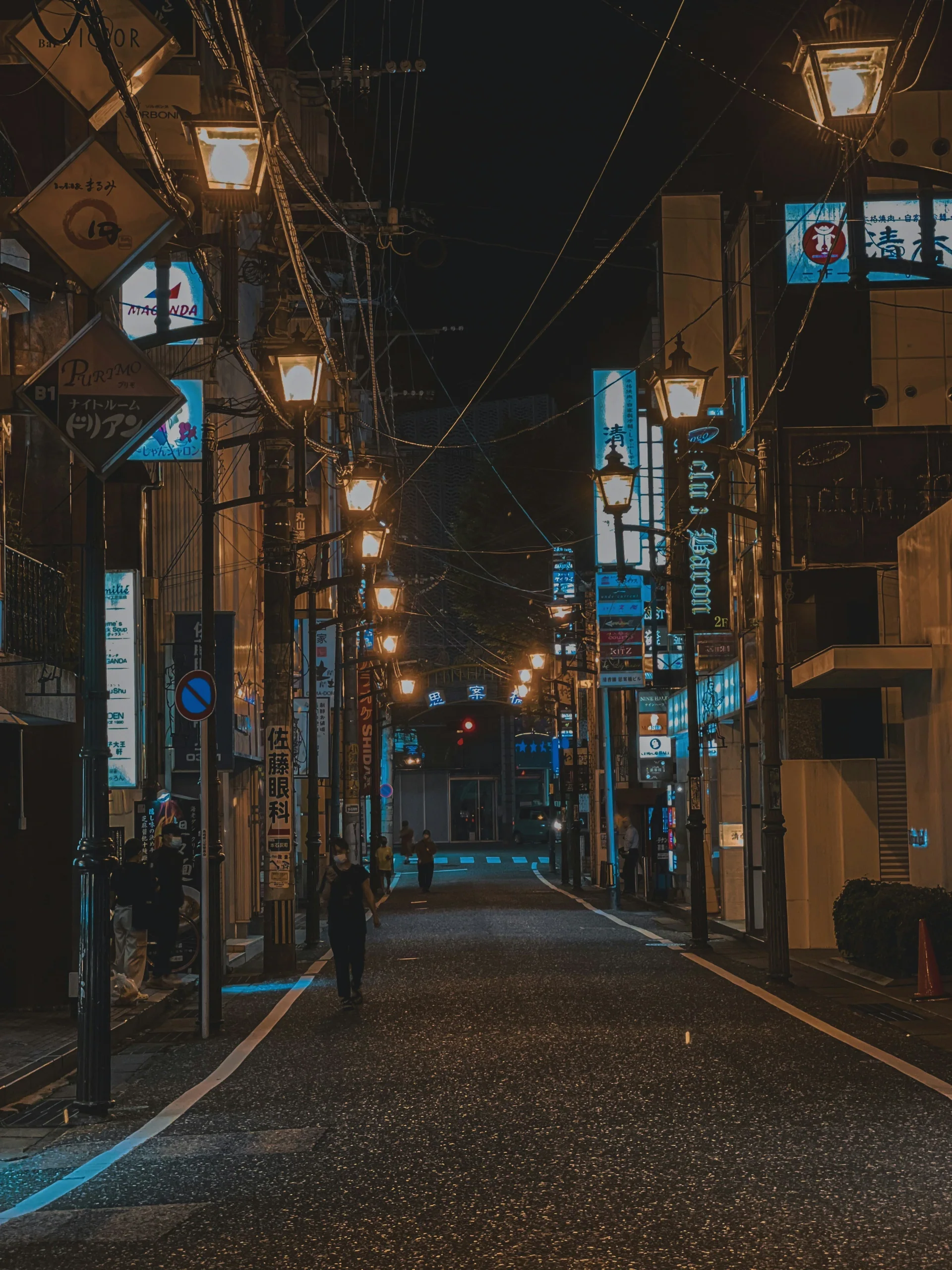 長崎市夜間街道兩旁的商店招牌與路燈，遠處有行人