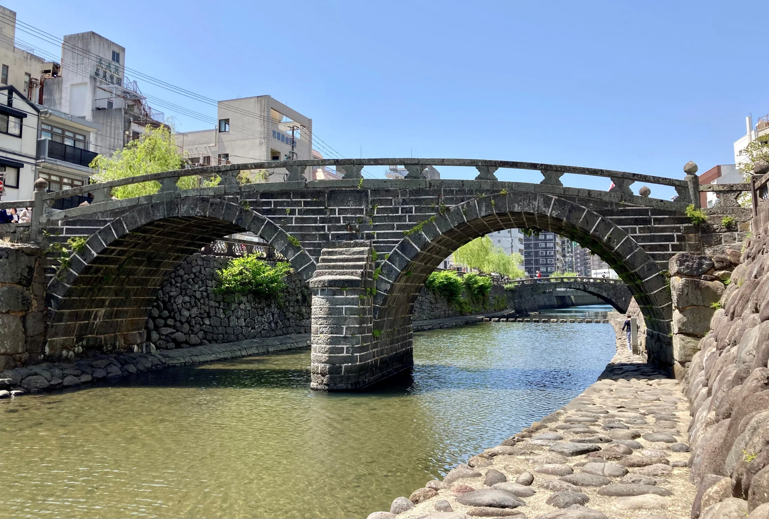 晴天時的長崎眼鏡橋橫跨中島川，兩道石拱與河岸同框
