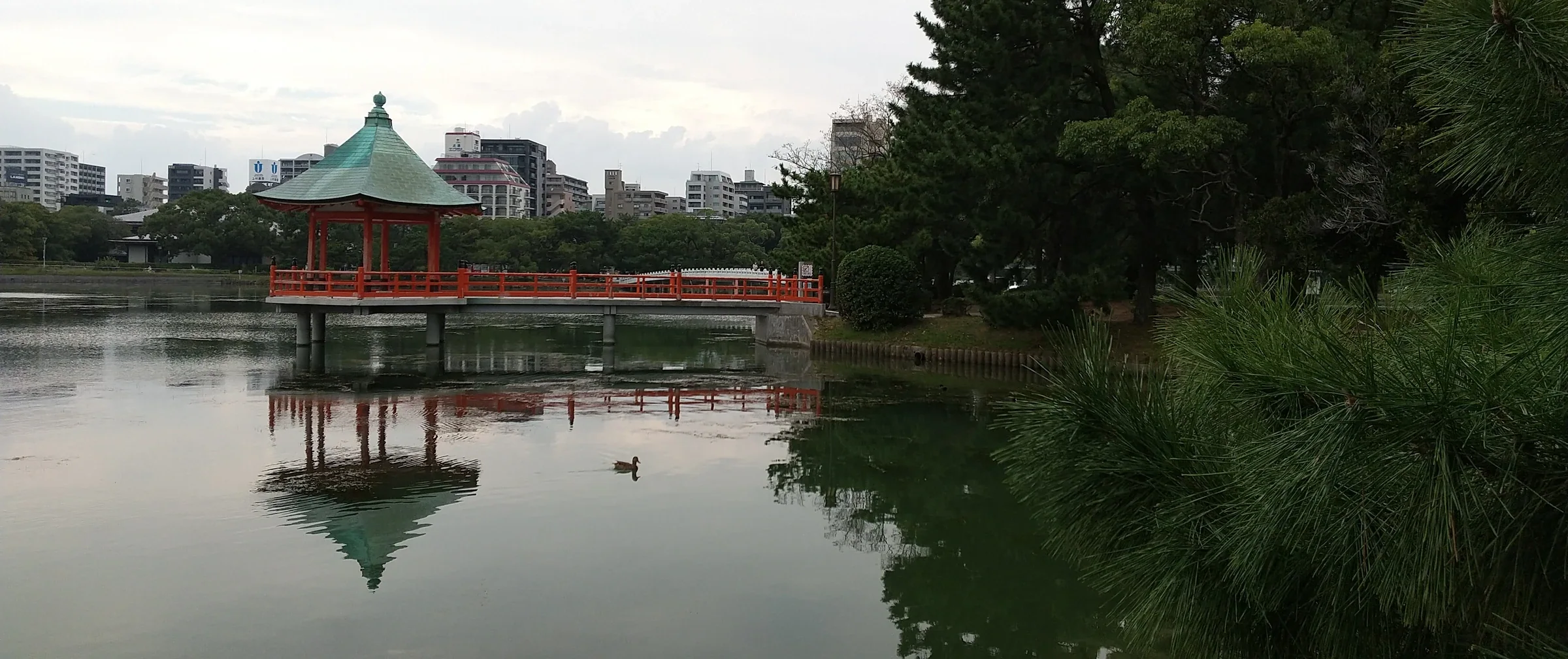 大濠池與浮見堂的寬幅實景，水面倒映紅色亭橋，周圍是公園樹木