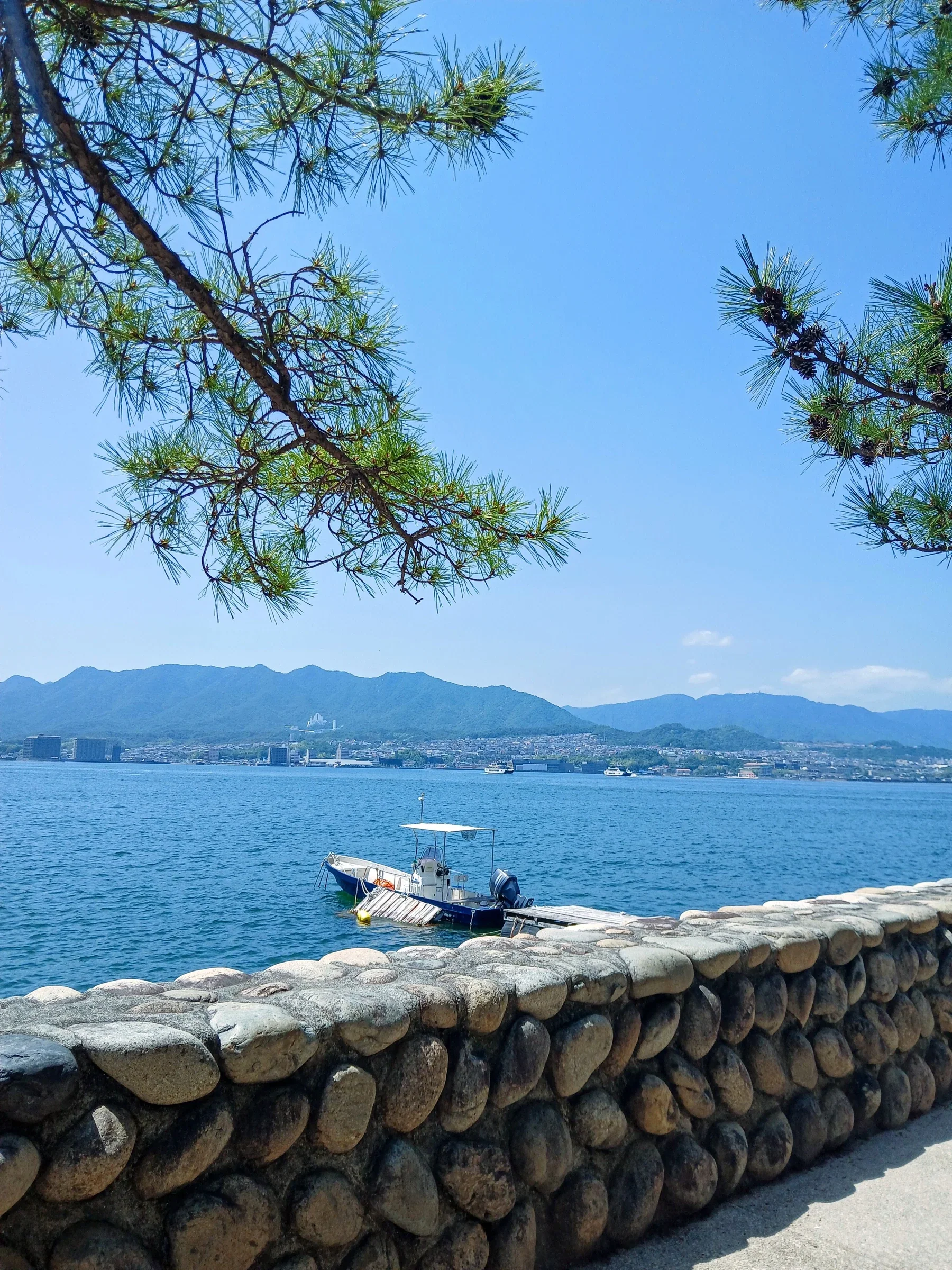 佐世保灣海邊石牆、遊艇與對岸山巒
