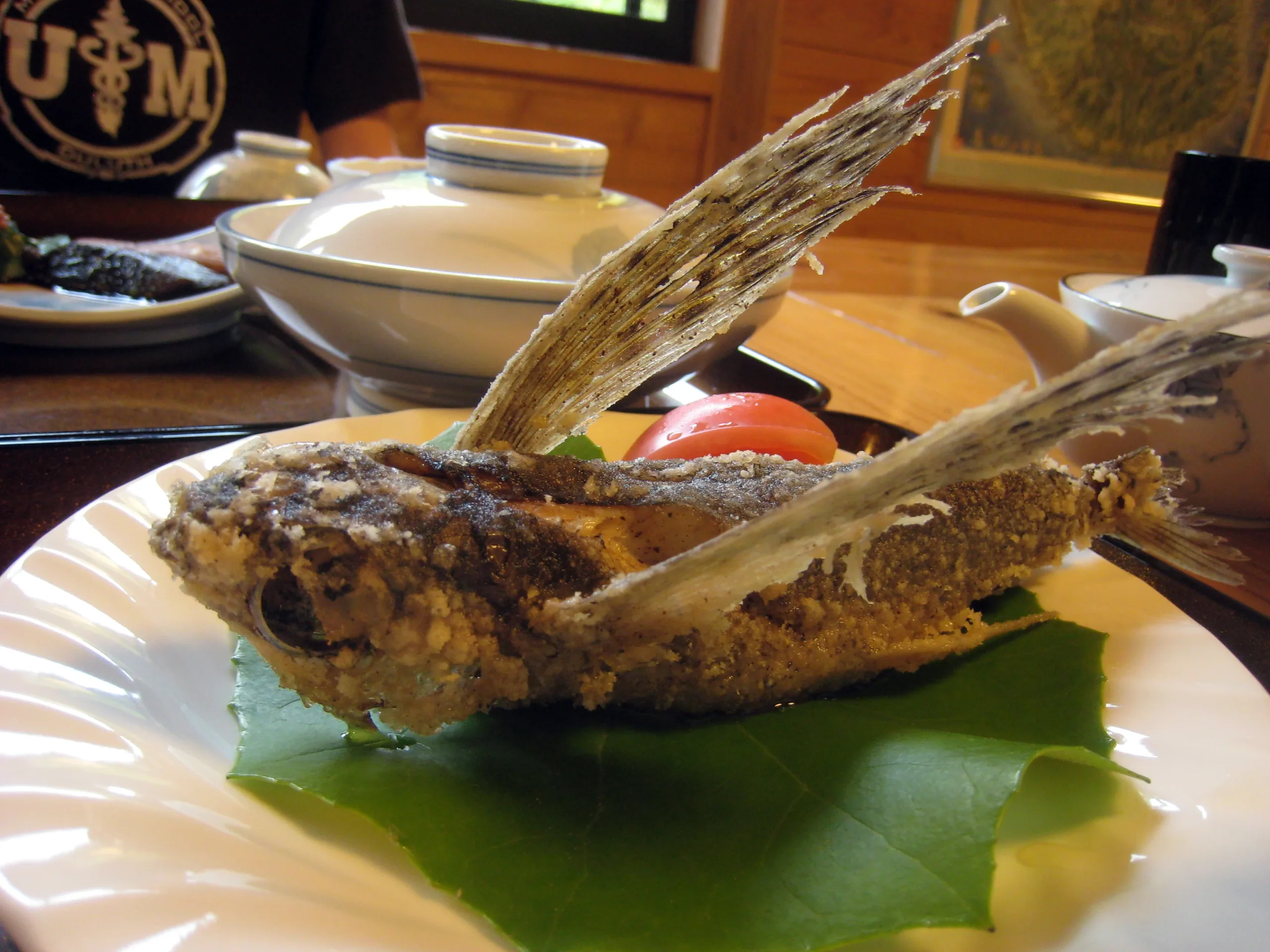 屋久島旅館晚餐中的整尾飛魚唐揚，魚鰭展開置於白色餐盤上，背景可見餐桌器皿