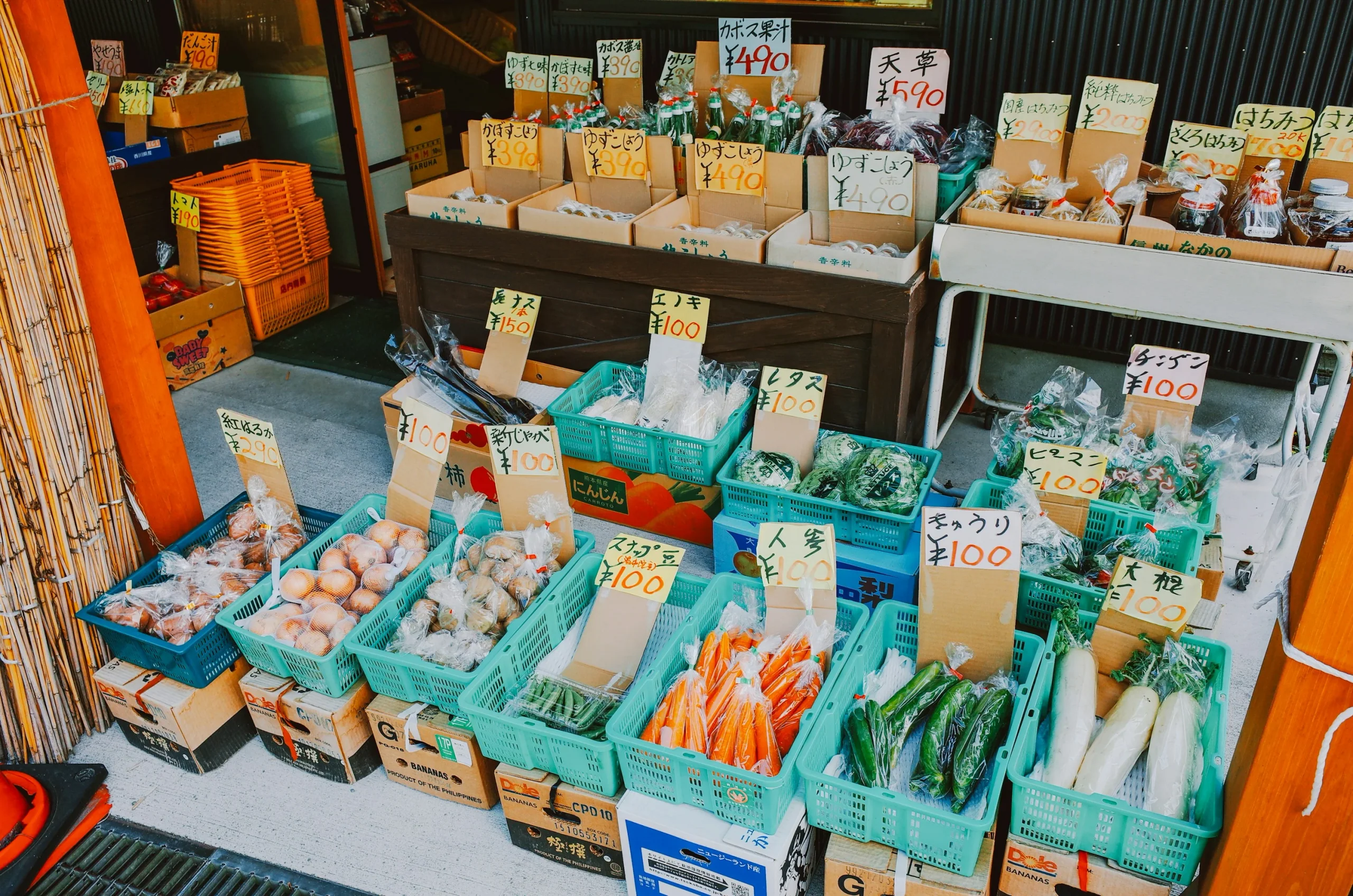由布院戶外攤位陳列蔬菜與食品，前方有手寫價牌